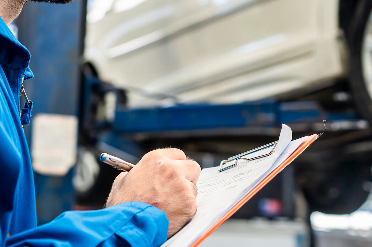 Vehicle service maintenance young handsome man check car condition on lifter in garage. Automotive mechanic male write check items in motor maintenance checklist document. Car repair service concept